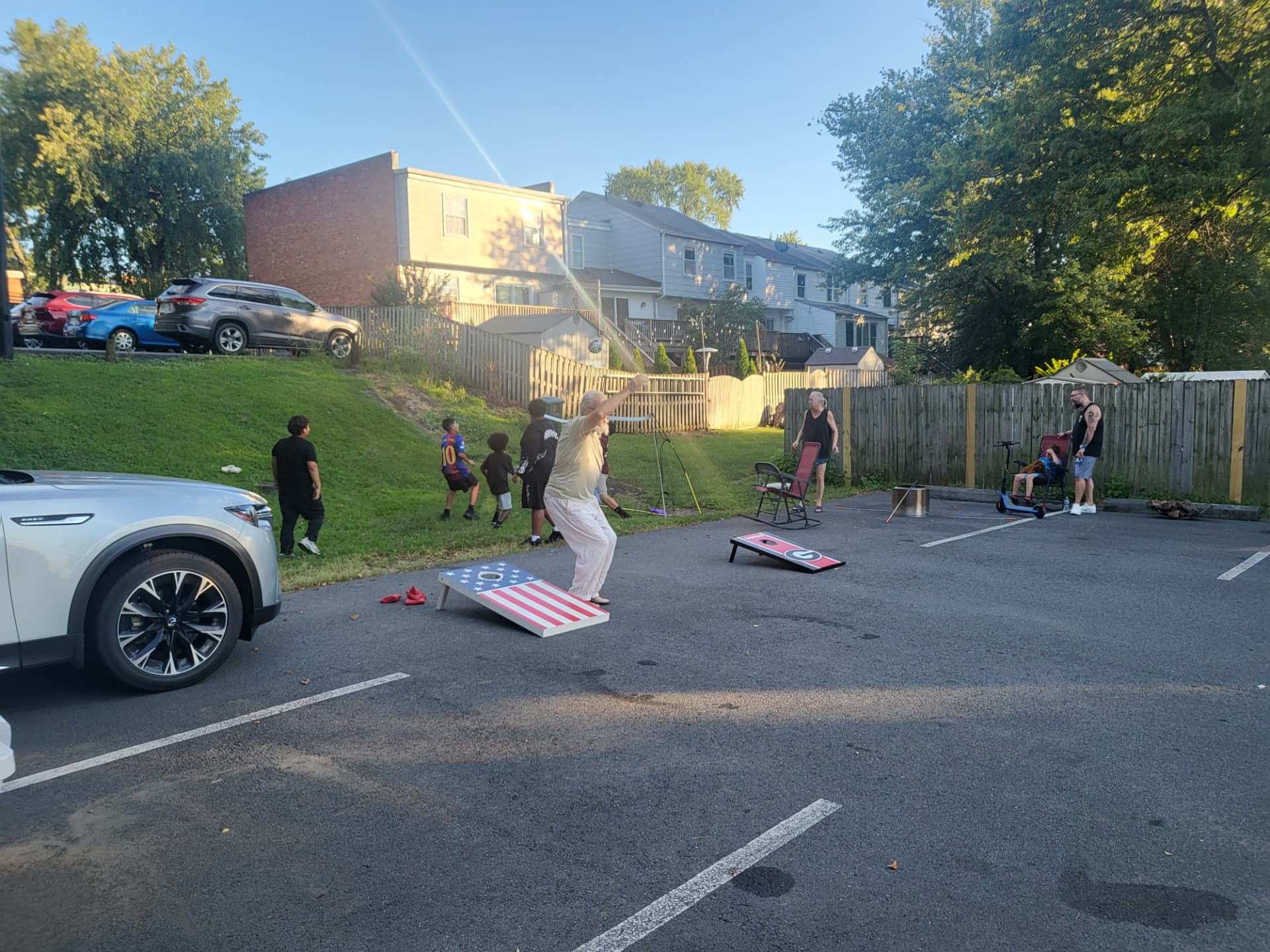 A resident tossing a cornhole bag while kids watch nearby